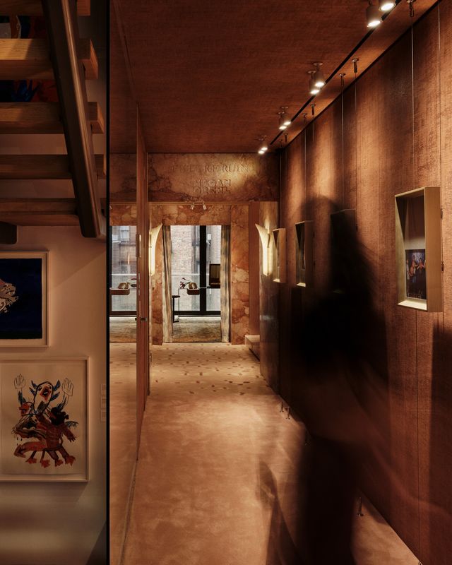 corridor with a passing figure, framed photographs and a stone stair