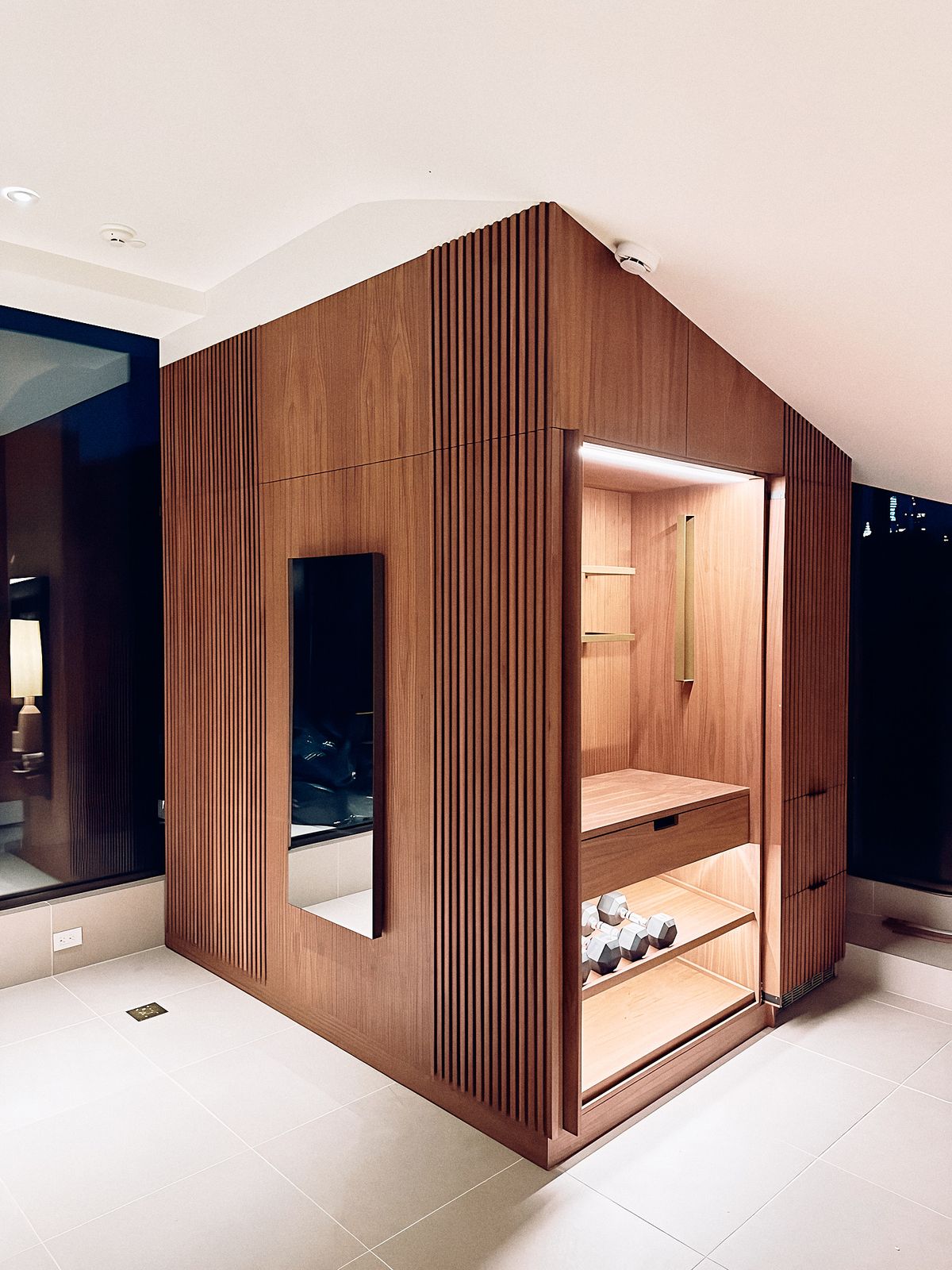slat wall open beside the screen, bay lit from above with rails and dumbbells